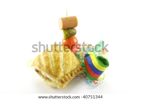 Small sausage roll with party blower and cocktail stick containing hot dog sauage, gherkin and tomato on a reflective white background