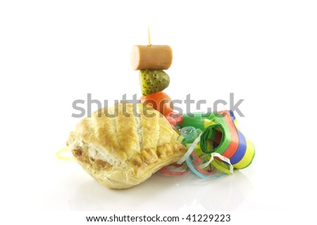 Small sausage roll with party blower and cocktail stick containing hot dog sauage, gherkin and tomato on a reflective white background