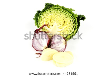 Half a raw green cabbage with a red onion cut in half and peeled potato slices on a reflective white background