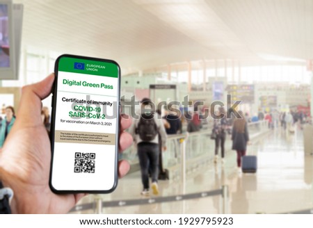 The digital green pass of the european union with the QR code on the screen of a mobile held by a hand with blurred airport in the background. Immunity from Covid-19. Travel without restrictions.