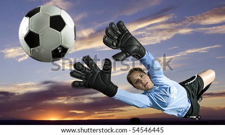 Soccer goalie blocks ball against sunset backdrop. Horizontal shot.