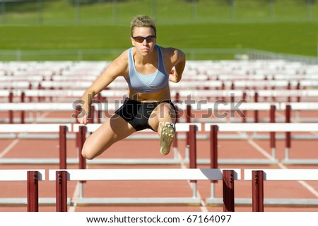 Track and field athlete jumps over hurdles.