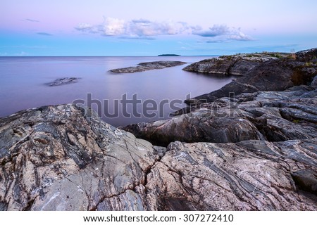 Long exposure of sunset landscape with subtle pink cast on cloudy sky and complex geological pattern on granite rocks in foreground at the island Patakansaaret in Ladoga lake, Karelia, Russia