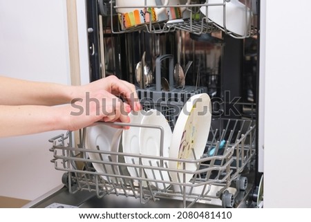 Female hands put dirty dishes in the dishwasher. Close-up of the dishes placed in the dishwasher. Automatic dishwashing machine at home. Household chores. Selective focus