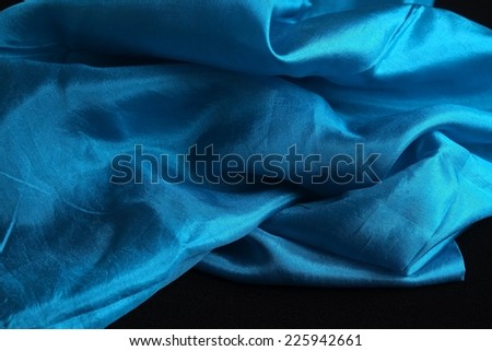 Smooth and shiny blue silk handkerchief on black velvet surface