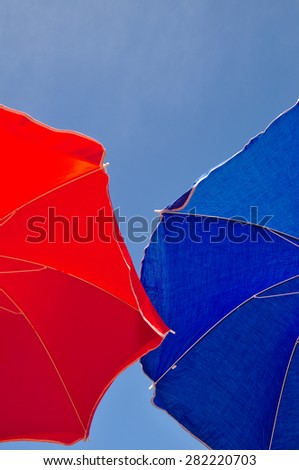 Red and blue beach umbrella and blue sky above. Summer beach vacations