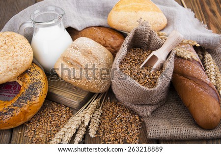 Different bread with wheat in a small bag and milk on a wooden background