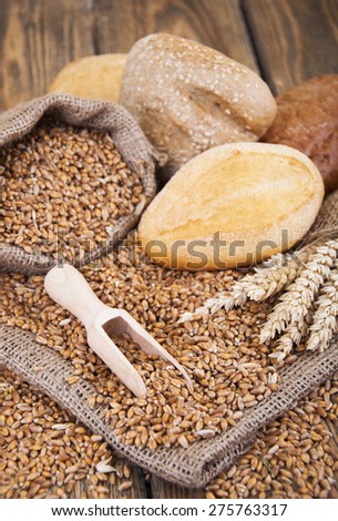 wheat grain in a small bag and different bread on a wooden background
