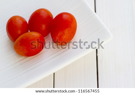 Four little red tomatoes over a white plate (focus on the tomato on the right, in the middle of image)