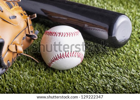 A baseball over green grass with bat and glove