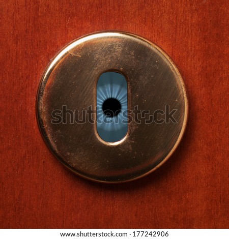 Blue eye behind a keyhole of a wooden door