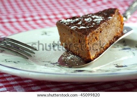 Piece of cake (pumpkin and pine, with icing sugar) on silver cutlery, white plate and red and white tablecloth