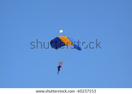Skydiver with blue and yellow parachute seen from back, with blue sky