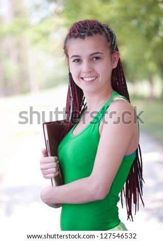 cheerful student girl with african braids keeping books, outside