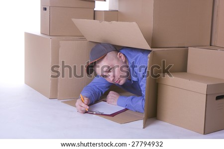 man in blue shirt and baseball cap looking out of carton box and writing on clipboard