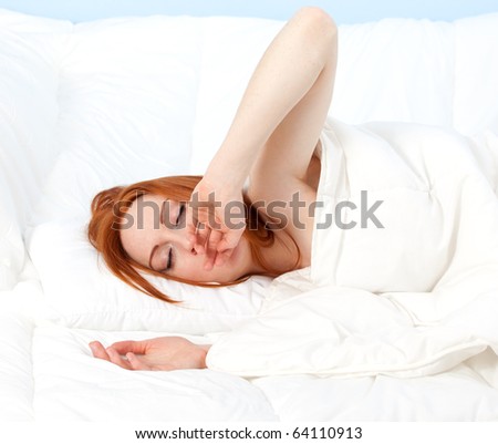 yawning beautiful young woman relaxing in white bedding