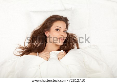 smiling beautiful young woman relaxing in white bedding