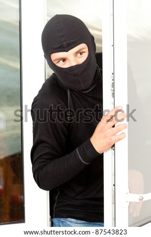 burglar  in mask and balaclava breaking into a house through window