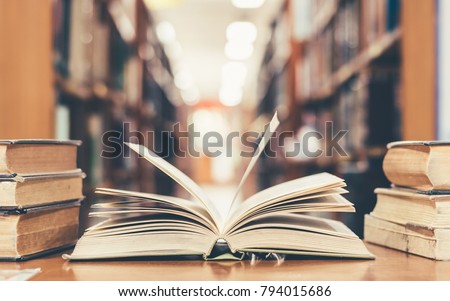Education learning concept with opening book or textbook in old library, stack piles of literature text academic archive on reading desk and aisle of bookshelves in school study class room background Foto stock © 