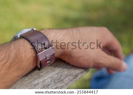 Sitting man\'s arm wearing brown leather watch