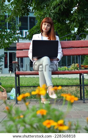 Girl in white dress sitting on a bench with a laptop on his knees