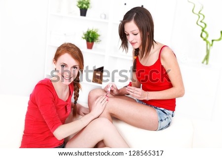 Pretty girl putting on nail polish to her smiling friend