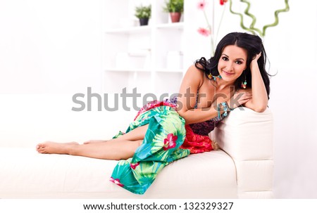Smiling young woman in colorful summer dress lying on the sofa at home