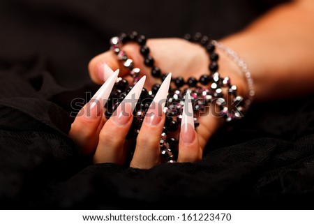 A woman\'s hand with sharp nails holding beads