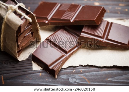Pieces of chocolate with packing paper on wooden table, rustic style