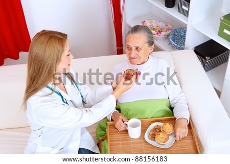 Lovely nurse helping old woman eating cookies