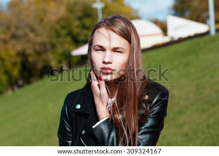 The beautiful young thin girl the teenager in a black leather jacket on the street in a sunny day