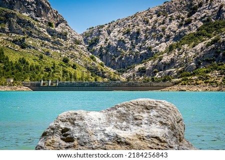 Front view of Mallorca largest barrage at reservoir Embassament de Cúber between mountains of mountain range Serra de Tramuntana with canyon and torrent d'Aumadrá behind and a stone in the foreground. Foto stock © 