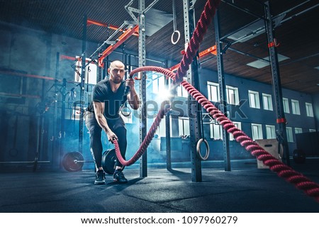 Men with battle rope battle ropes exercise in the fitness gym. CrossFit concept. gym, sport, rope, training, athlete, workout, exercises concept