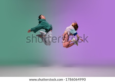 High jump. Boy and girl dancing hip-hop in stylish clothes on colorful gradient background at dance hall in neon. Youth culture, movement, style and fashion, action. Fashionable portrait. Street dance Foto stock © 