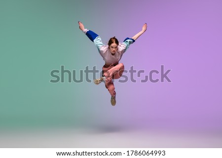 In jump. Beautiful girl dancing hip-hop in stylish clothes on colorful gradient background at dance hall in neon light. Youth culture, movement, style and fashion, action. Fashionable bright portrait. Foto stock © 