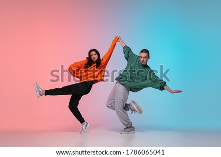 Boy and girl dancing hip-hop in stylish clothes on colorful gradient background at dance hall in neon. Youth culture, movement, style and fashion, action. Fashionable bright portrait. Street dance.