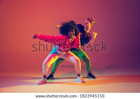 Stylish man and woman dancing hip-hop in bright clothes on green background at dance hall in neon light. Youth culture, hip-hop, movement, style and fashion, action. Fashionable portrait.