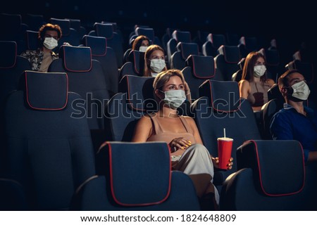 Cinema in quarantine. Coronavirus pandemic safety rules, social distance during movie watching. Men, women in protective face mask sitting in a rows of auditorium. Leisure time, youth culture concept. Imagine de stoc © 