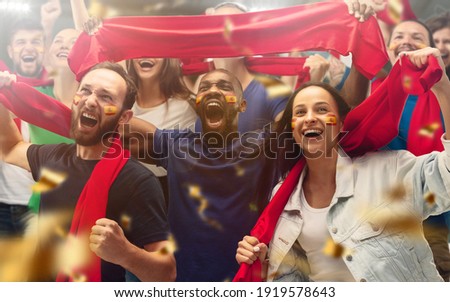 Spainian football, soccer fans cheering their team with a red scarfs at stadium. Excited fans cheering a goal, supporting favourite players. Concept of sport, human emotions, entertainment.