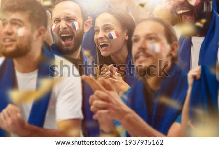Francian football, soccer fans cheering their team with a blue scarfs at stadium. Excited fans cheering a goal, supporting favourite players. Concept of sport, human emotions, entertainment.