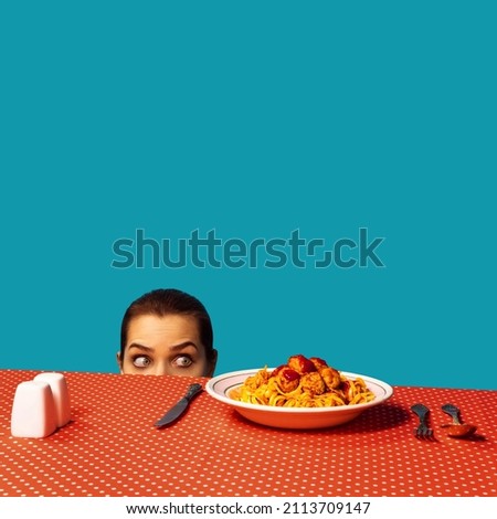 Young girl spying on spaghetti with meatballs on plaid tablecloth isolated on bright blue background. Food pop art photography. Vintage, retro style interior. Complementary colors, Copy space for ad Foto stock © 