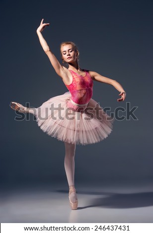 Portrait of the ballerina in ballet pose on a grey background. Ballerina is wearing  pink tutu and pointe shoes