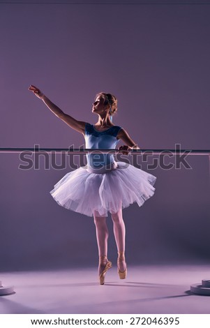 classic ballet dancer in white tutu at ballet barre on a lilac background