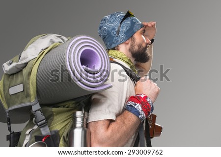 Portrait of a male fully equipped tourist with backpack and the camera on gray background. side view. tourist looking into the distance