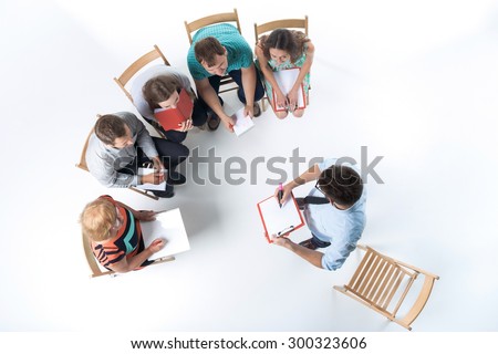 Top view of business people in a meeting on white background. all sitting with notepad and pen. speaker standing and writing in notebook