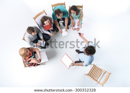 Top view of business people in a meeting on white background. all sitting with notepad and pen. speaker standing and saying something