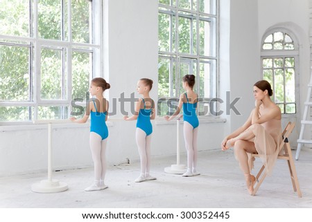 Three little ballerinas with personal classic ballet teacher in dance studio posing at ballet barre on a white background