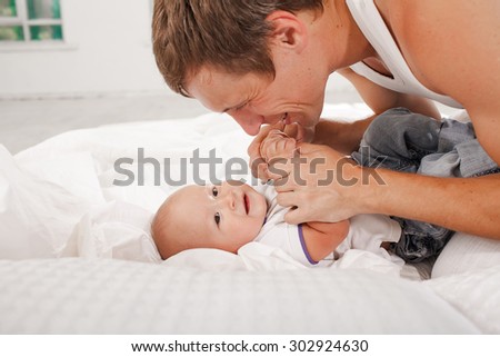 Young smiling father with his nine months old son on the bed at home on white home background