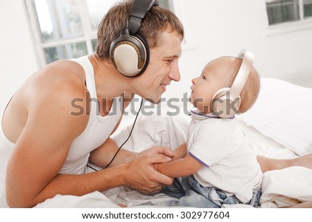 young father with his nine months old som on the bed at home on white background. Father and son wearing headphones