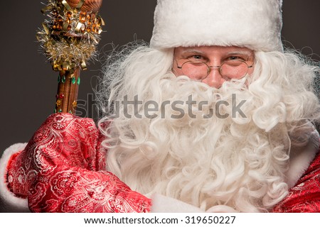 happy Santa Claus in eyeglasses with staff looking at camera on black background